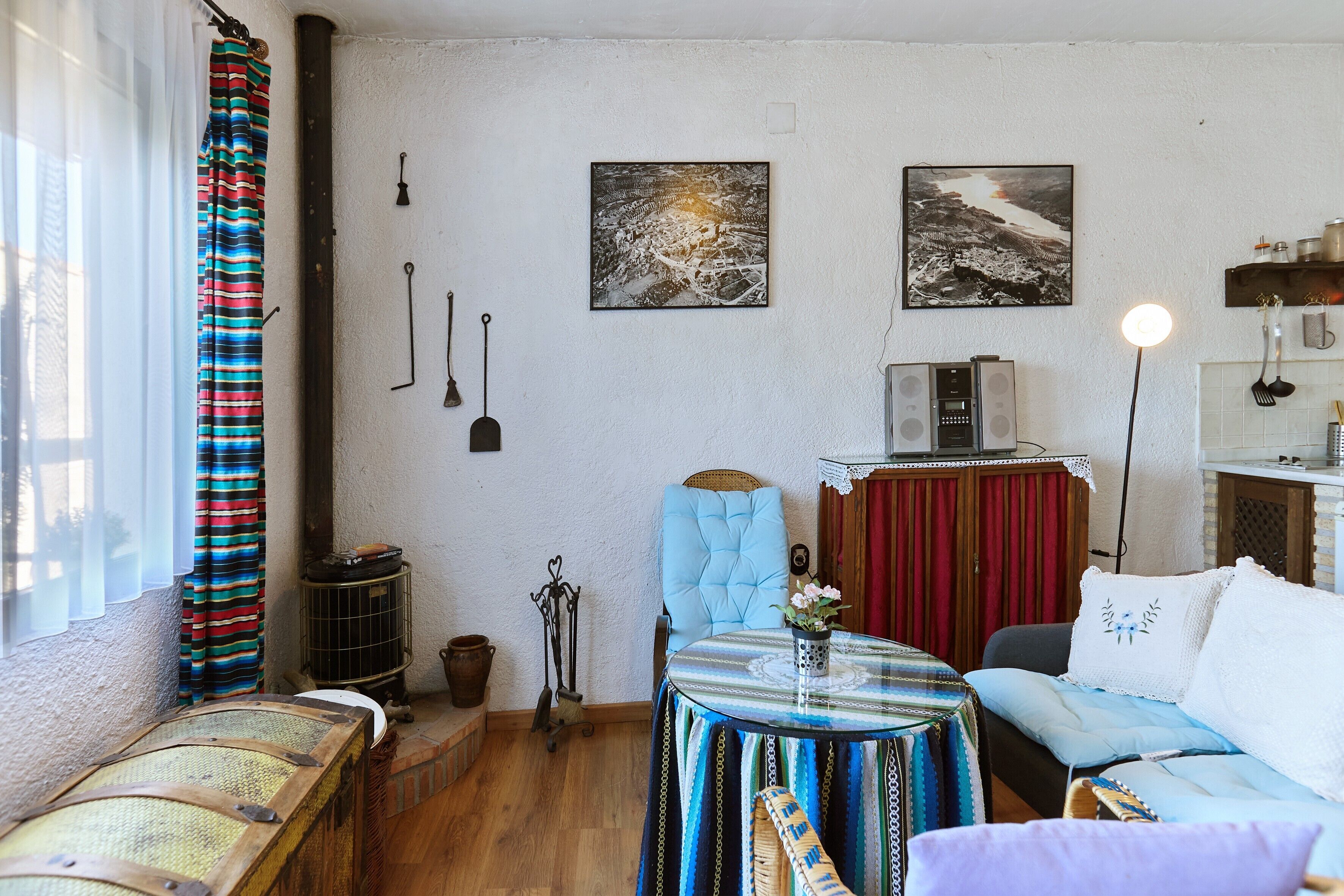 Un salon chaleureux avec un canapé, une table sur laquelle est posé un vase, et un fauteuil. Il y a deux tableaux au mur, une fenêtre avec des rideaux et un radiateur.
