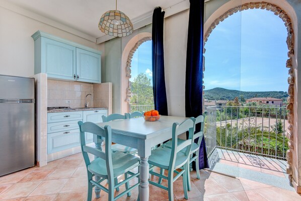A kitchen with a dining table and chairs, a refrigerator, and a view through an archway. - Studio Apartment 'Monolocale Castle' with Shared Pool, Wi-Fi and Air Conditioning (Campo nell'Elba)