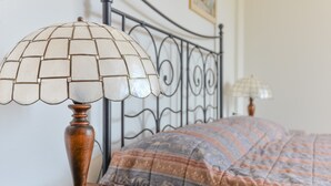 A bed with a patterned bedspread, a wooden bedside table, a lamp with a white shade, and a book. - Studio Apartment 'Monolocale Castle' with Shared Pool, Wi-Fi and Air Conditioning (Campo nell'Elba)
