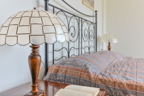 A bed with a patterned bedspread, a wooden bedside table, a lamp with a white shade, and a book. - Studio Apartment 'Monolocale Castle' with Shared Pool, Wi-Fi and Air Conditioning (Campo nell'Elba)