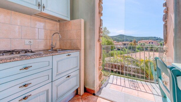 A kitchen with light blue cabinets and a view of a balcony with a railing. - Studio Apartment 'Monolocale Castle' with Shared Pool, Wi-Fi and Air Conditioning (Campo nell'Elba)