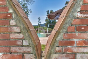 Een bakstenen muur met een helder uitzicht op een zwembad en een pergola op de achtergrond.