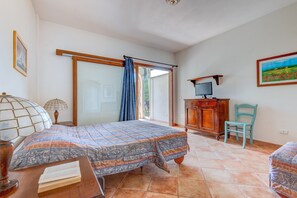 Een slaapkamer met een bed, een bureau, een stoel, een televisie en een schuifdeur.'