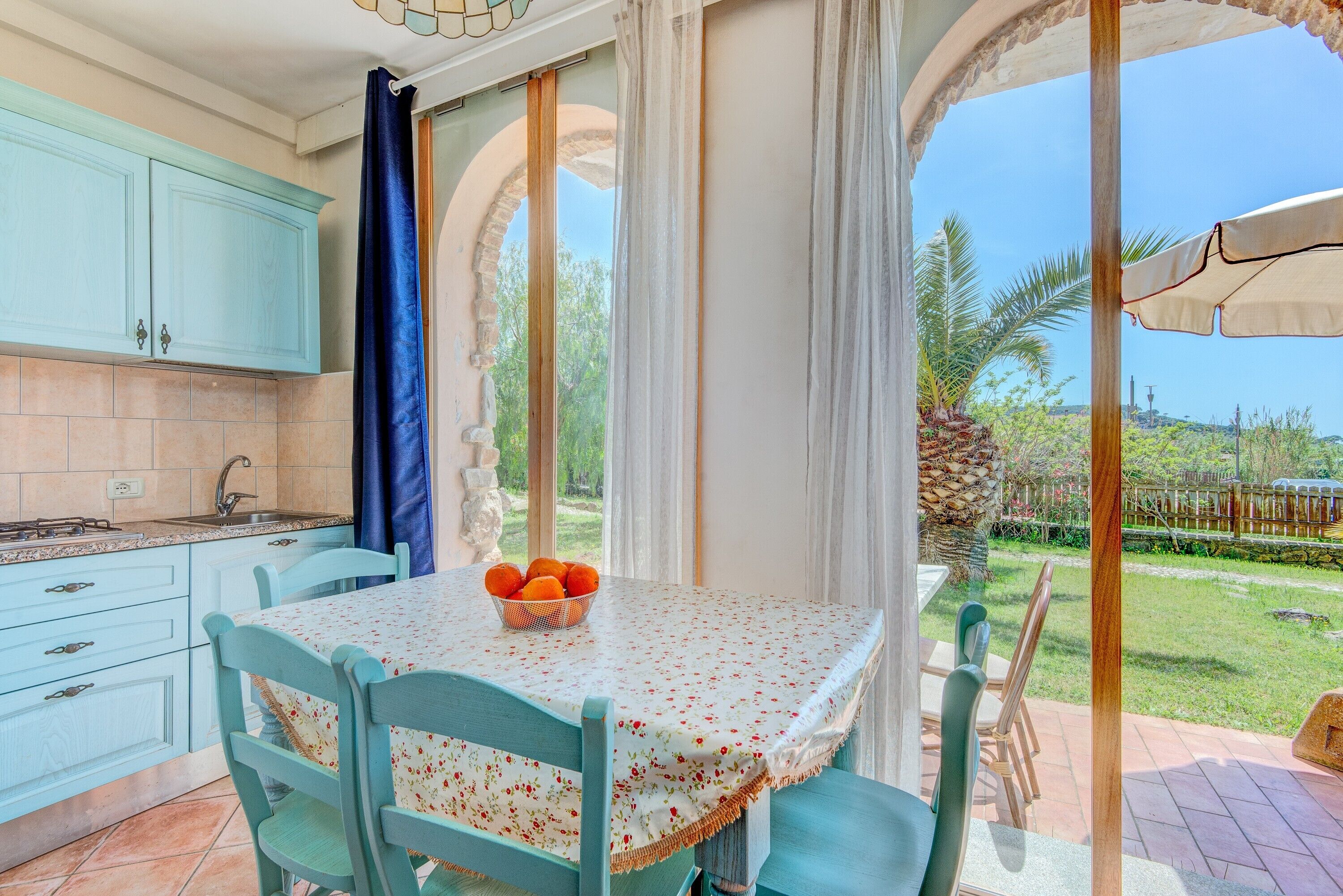 A kitchen with light blue cabinets, a dining table with a floral tablecloth, and a bowl of oranges.
