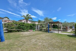 Un espace extérieur verdoyant avec une aire de jeux, un espace de repos couvert et un bâtiment en arrière-plan.