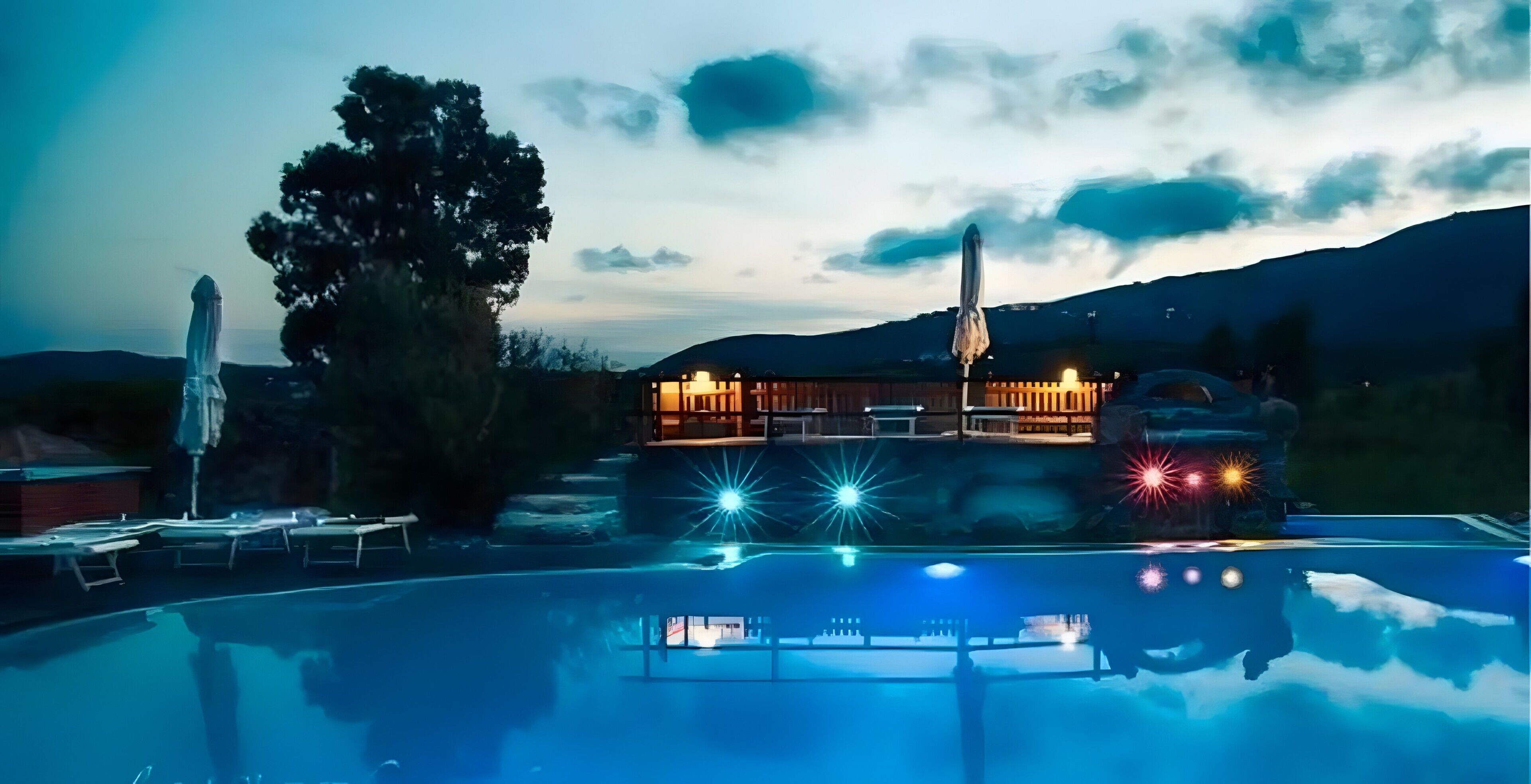 A pool area with a building in the background, a tree, and a mountain range.