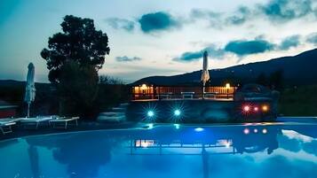 A pool area with a building in the background, a tree, and a mountain range.