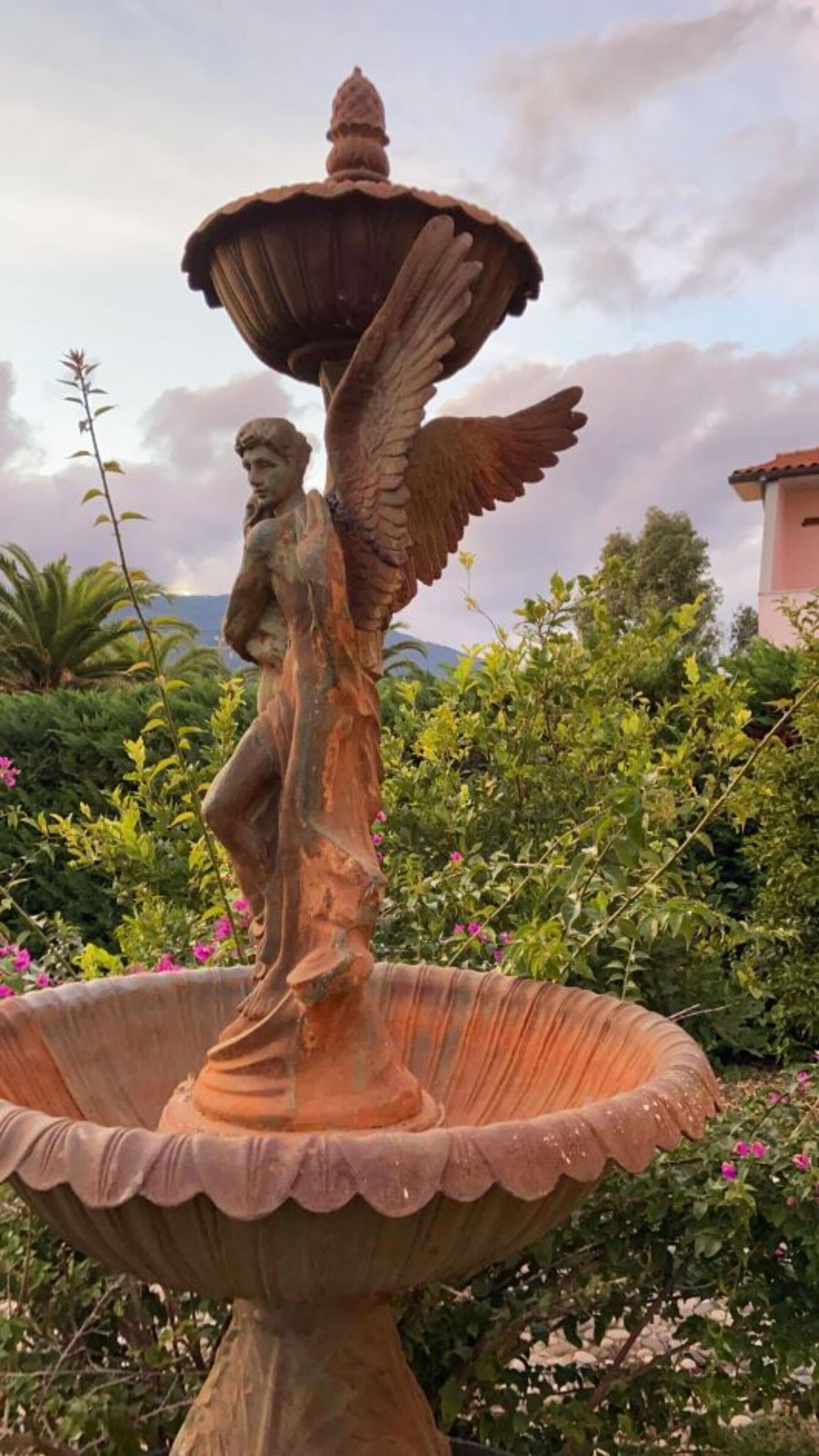 A garden with a statue of a winged figure on a pedestal.