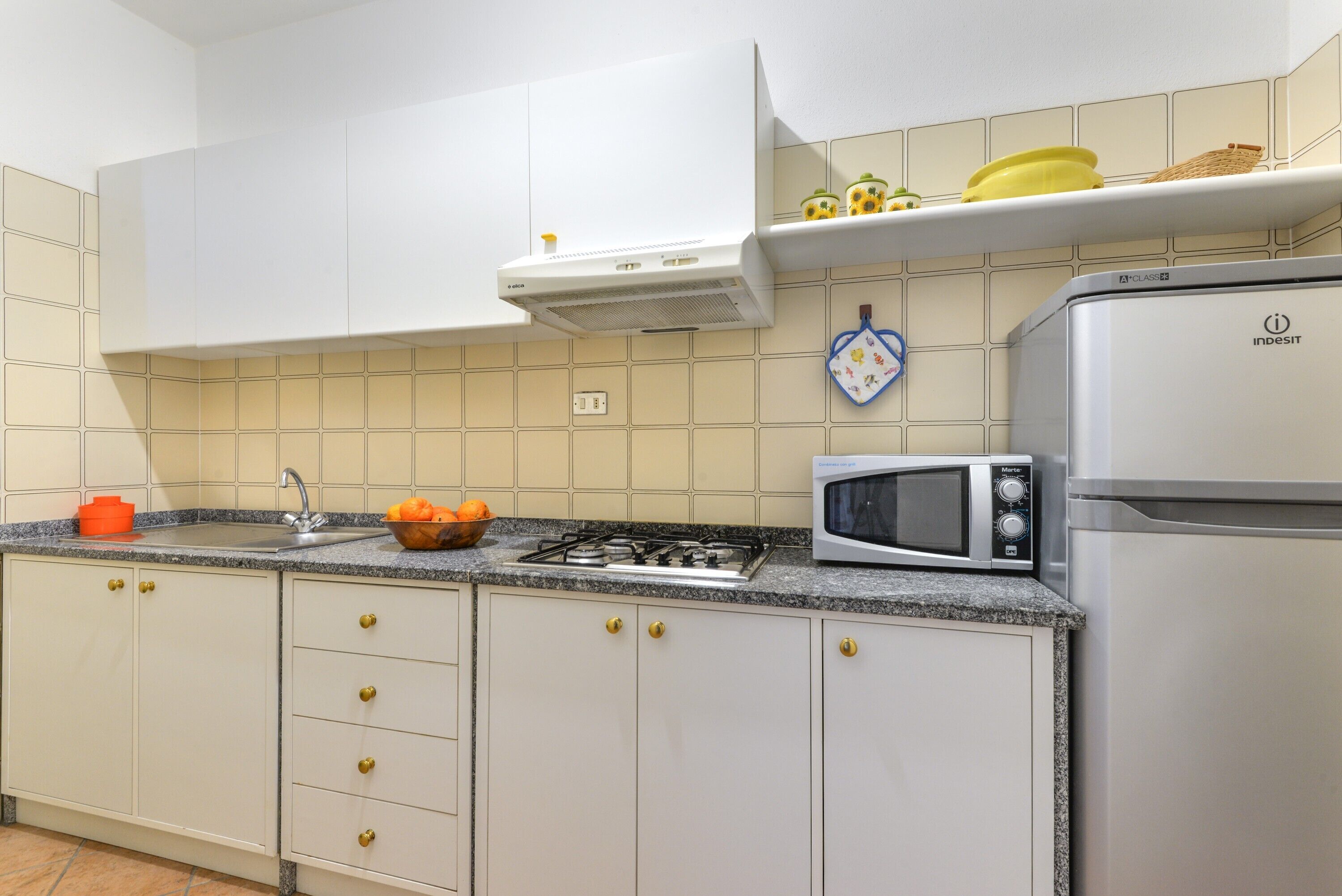 Una cocina con armarios blancos, estufa a gas, microondas y refrigerador.