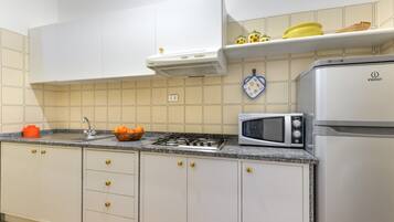 Una cocina con armarios blancos, estufa a gas, microondas y refrigerador.