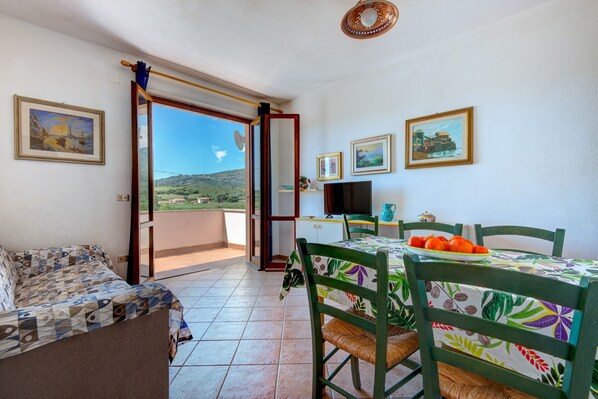 Ein Zimmer mit einem Bett, einem Esstisch mit Stühlen, einem Fernseher und einem Balkon mit Blick auf die Landschaft.
