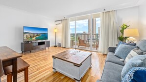 Un salón espacioso con suelo de madera, un sofá gris, una mesa de centro y un televisor que muestra una vista panorámica.