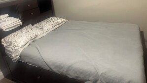 A neatly made bed with a patterned pillow and a folded towel on a dark wooden headboard. - Charming 2-bedroom house in awesome Edmonton with AC, WiFi (Edmonton)
