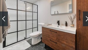 A modern bathroom with a shower enclosure, a toilet, a vanity with a mirror, and a wooden cabinet. - Charming 2-bedroom house in awesome Edmonton with AC, WiFi (Edmonton)