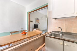 Una cocina pequeña con una mesa de madera, un cuenco de fruta y un lavamanos.