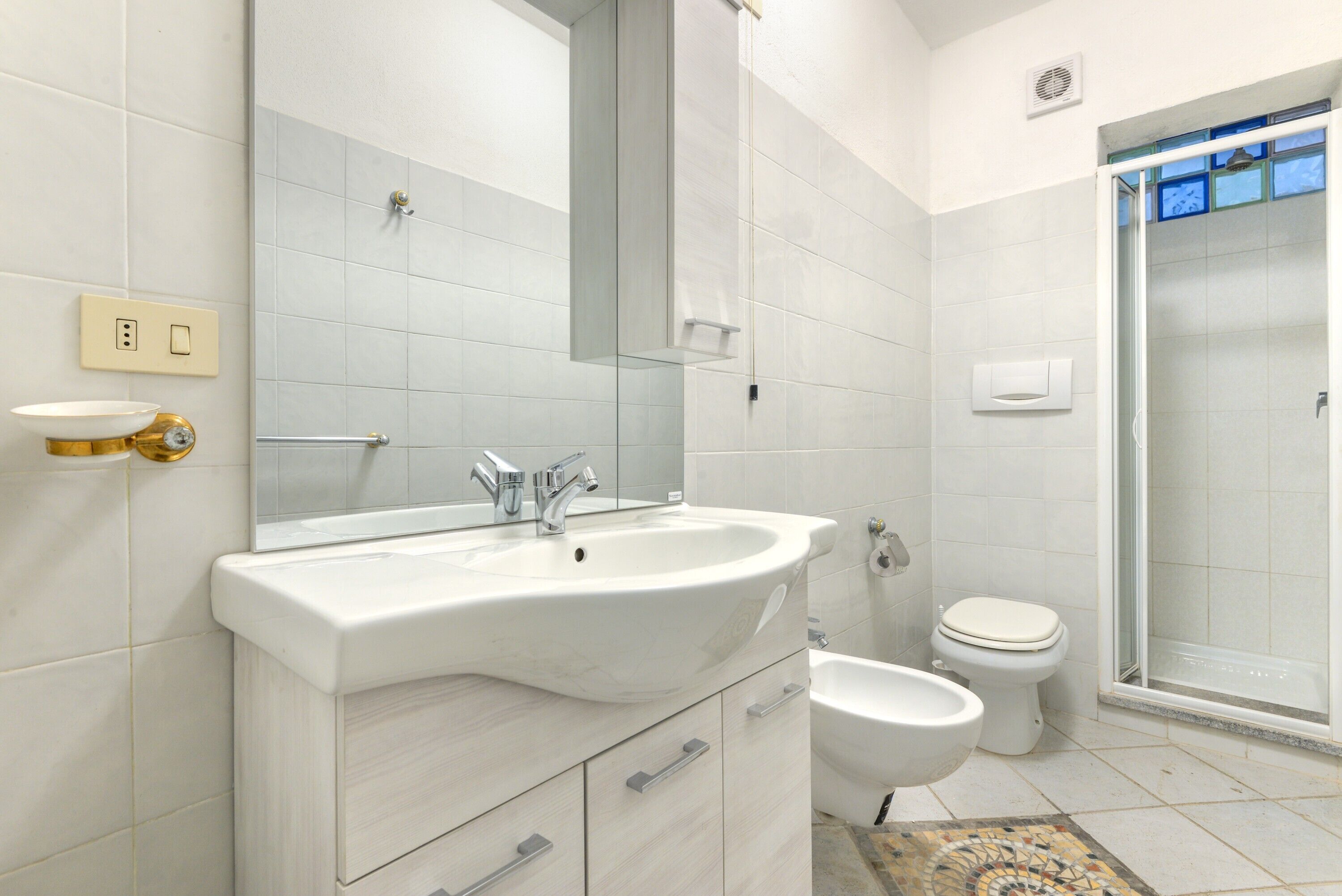 A bathroom with a sink, mirror, toilet, bidet, and shower.