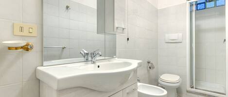 A bathroom with a sink, mirror, toilet, bidet, and shower.