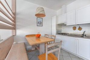 Une cuisine avec des meubles blancs, une table en bois et un luminaire suspendu.