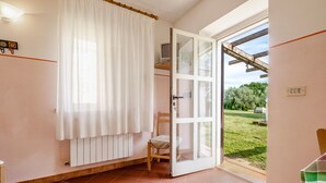 A room with a sliding glass door to a garden, a chair, a radiator, and a clock on the wall. - Apartment 'Porcilaia' with Shared Pool, Private Terrace and Shared Garden (Sorano)