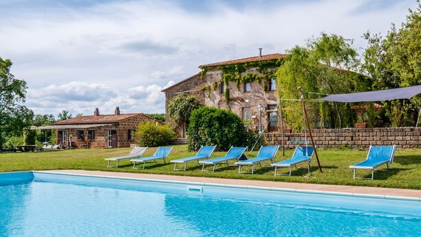 A swimming pool with blue lounge chairs, a stone building with ivy, and a clear sky. - Apartment 'Porcilaia' with Shared Pool, Private Terrace and Shared Garden (Sorano)
