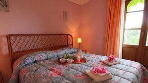 A bed with a floral bedspread, a bedside lamp, and a window with curtains. - Apartment 'Pollaio' with Shared Pool, Private Terrace and Shared Garden (Sorano)