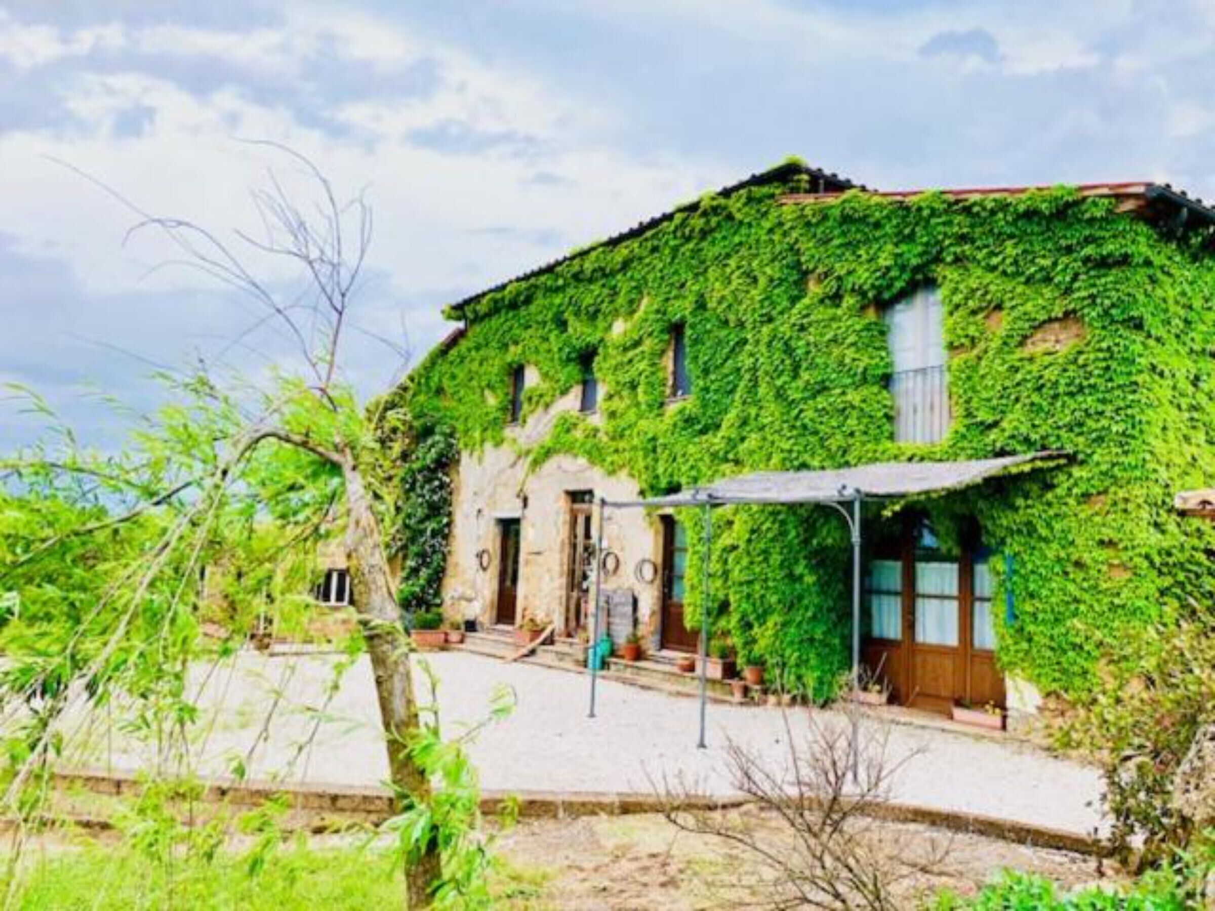 Un bâtiment à la façade en pierre, partiellement recouverte de lierre, avec une porte en bois et un petit porche.