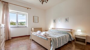 Un dormitorio con cama, mesitas de noche, una ventana con cortinas y un candelabro.