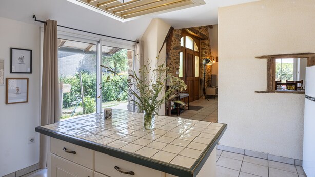 Una cocina con mostrador de baldosas, un jarrón con flores y vistas al exterior.