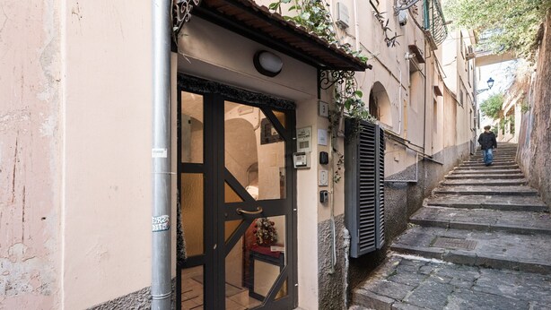 A narrow street with a building entrance, a metal pole, and a staircase leading up.