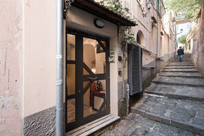 A narrow street with a building entrance, a metal pole, and a staircase leading up.