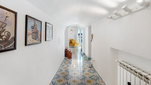A hallway with tiled flooring, framed artwork on the walls, and a staircase with a white railing.