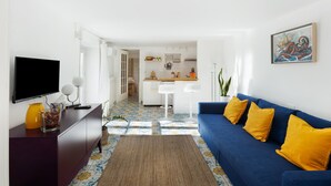 A living room with a blue sofa, a television, and a kitchen in the background.