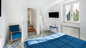 A bedroom with a bed, a chair, a TV, a window, and a staircase leading to another room.