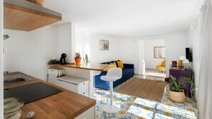 A modern kitchen with a wooden countertop, a dining area with a blue sofa, and a living room with a patterned floor.