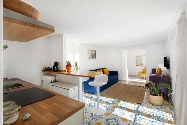 A modern kitchen with a wooden countertop, a dining area with a blue sofa, and a living room with a patterned floor.