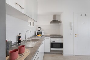 Moderni keittiö, jossa on valkoiset kaapit, ruostumattomasta teräksestä valmistettu pesuallas, mikroaaltouuni ja liesi.