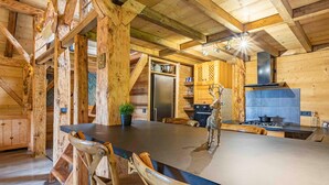 Un intérieur rustique en bois, avec une grande table à manger, des chaises, un réfrigérateur, des placards et une cheminée.