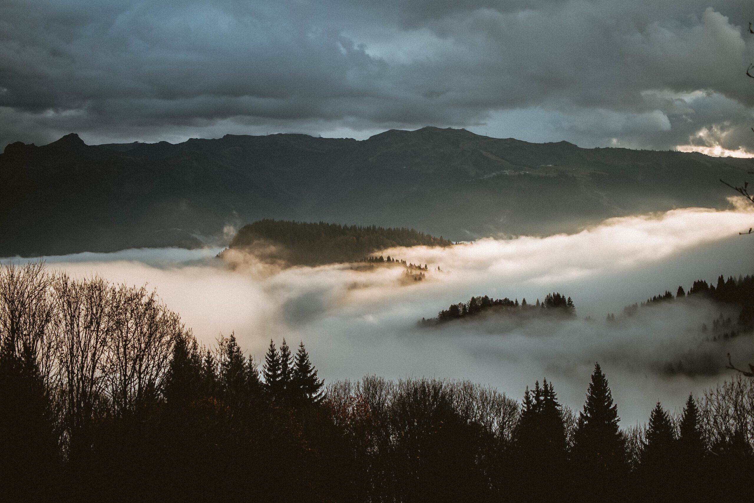 Un paysage montagneux, avec des zones boisées et une vallée enveloppée de brume.