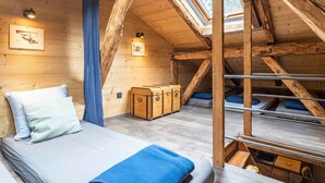 Une chambre mansardée chaleureuse avec un lit superposé, des poutres en bois, une lucarne et un petit coffre.