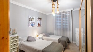 A bedroom with two beds, a ceiling fan, a nightstand, and a window with sheer curtains.