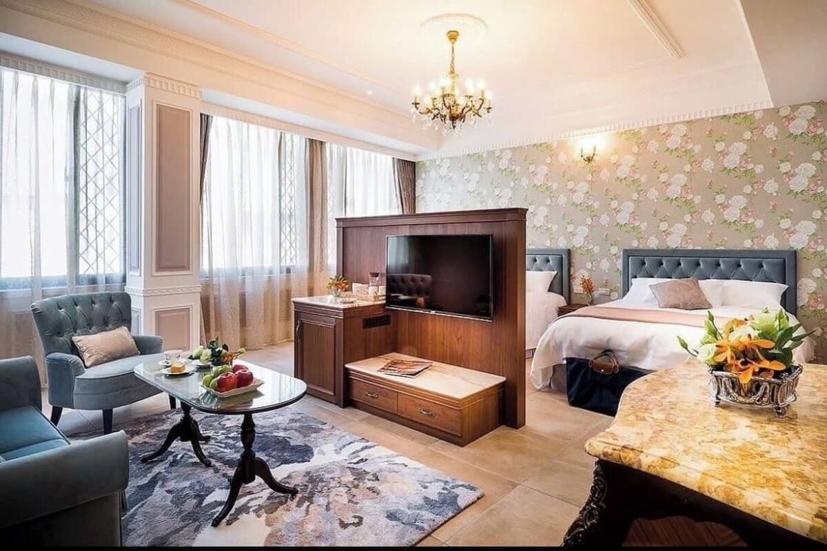 A hotel room with a large bed, a TV, a seating area with a table, and a chandelier.