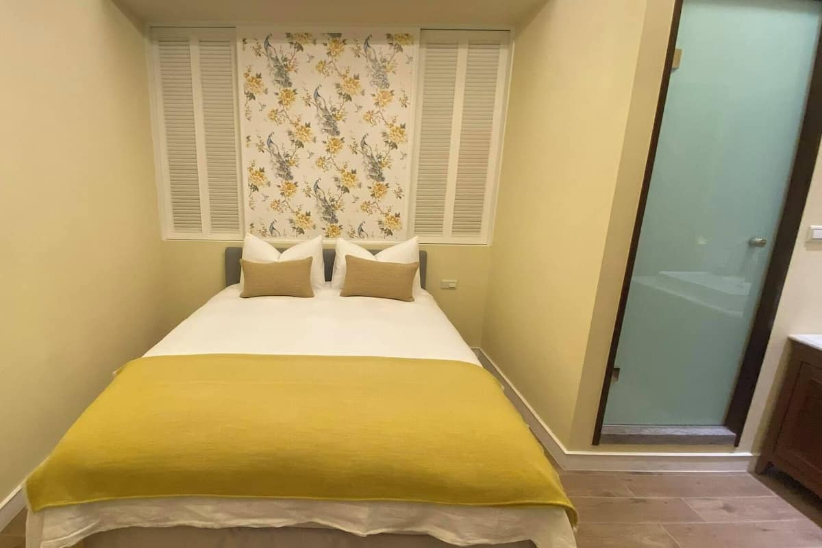 A small, narrow room with a bed, two pillows, and a yellow blanket.