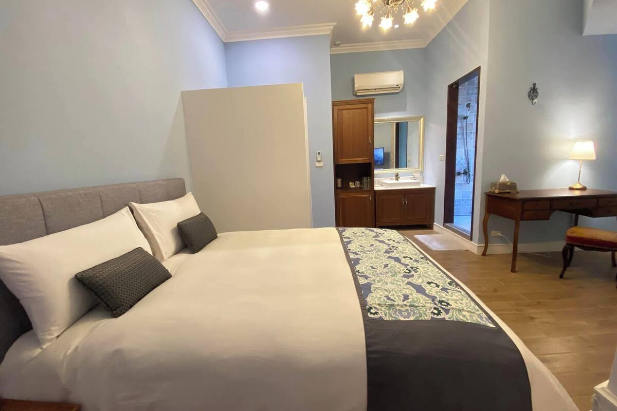 A bedroom with a bed, bedside table, and a desk with a lamp.