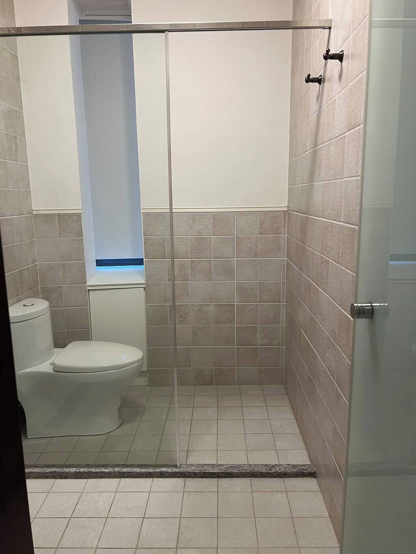 Une salle de bain comprenant des toilettes, un espace douche et des murs carrelés.