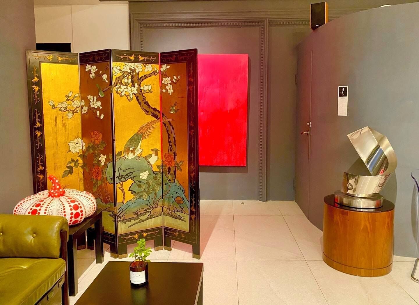 Une pièce décorée d’un paravent chinois traditionnel, d’une sculpture abstraite moderne et d’un canapé vert.