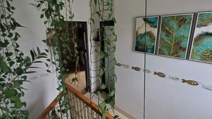 Una escalera con barandilla de madera, un muro con arte abstracto y plantas trepadoras verdes.