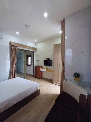Une chambre d’hôtel comprenant un lit, une télévision, une armoire en bois, une petite table avec une plante et une vitrine.