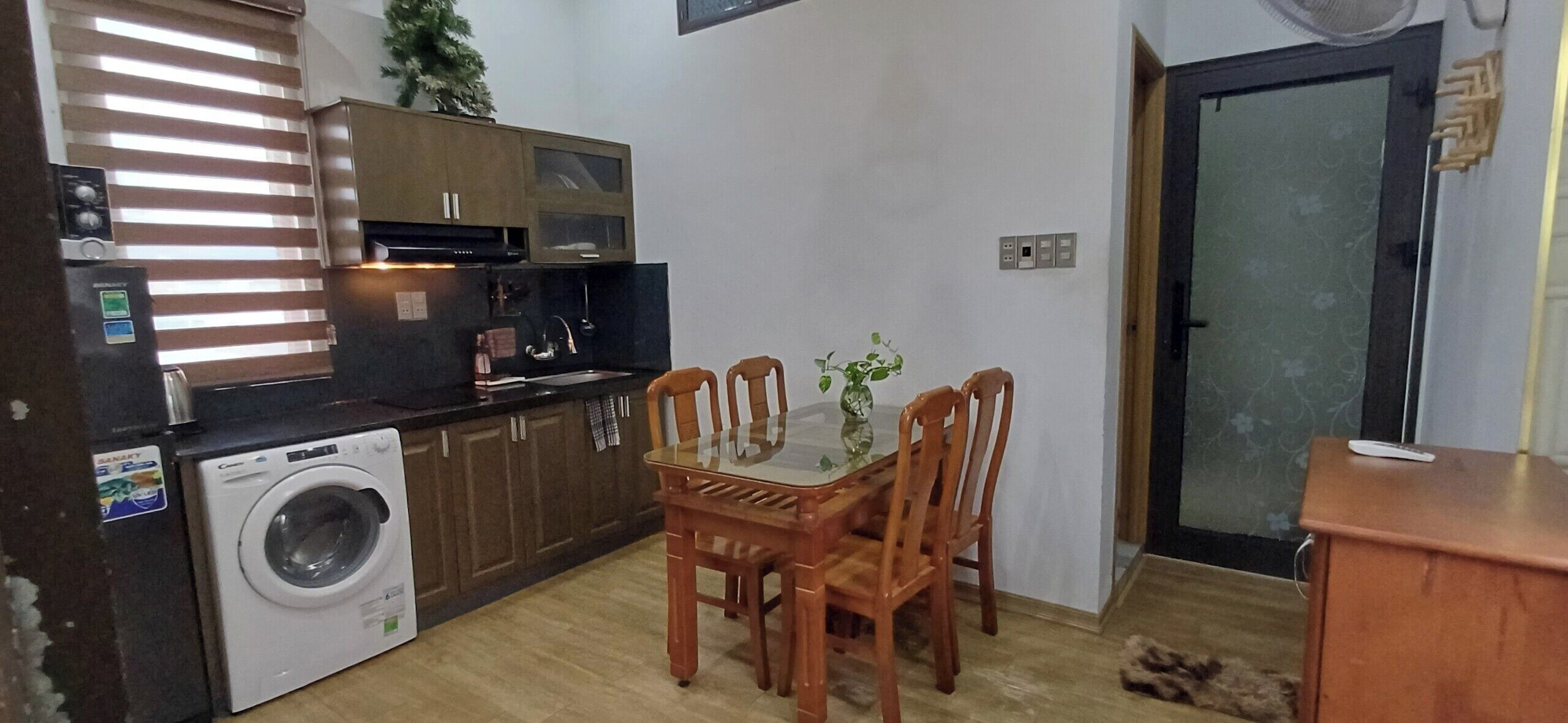 Una cucina funzionale con lavatrice, mobili in legno, un tavolo con sedie e una piccola pianta.