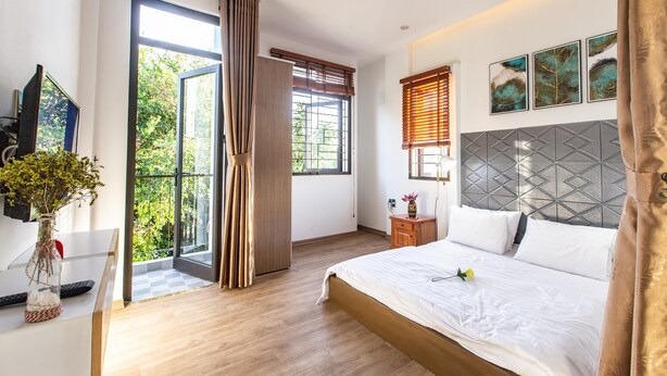 Un dormitorio moderno con una cama grande, una mesita de noche, una lámpara y vistas a zonas verdes por la ventana.