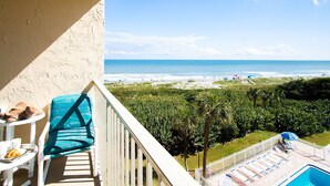 A balcony with a view of the beach and ocean, a pool area with lounge chairs, and a table with breakfast items. - Beautiful Condo w/ Heated Pool & Stunning Ocean Views in Cape Canaveral! 🌊 (Cape Canaveral)